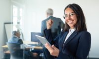 happy-female-professional-glasses-suit-holding-tablet-making-winner-gesture-while-two-businessmen-working-glass-wall-copy-space-communication-concept